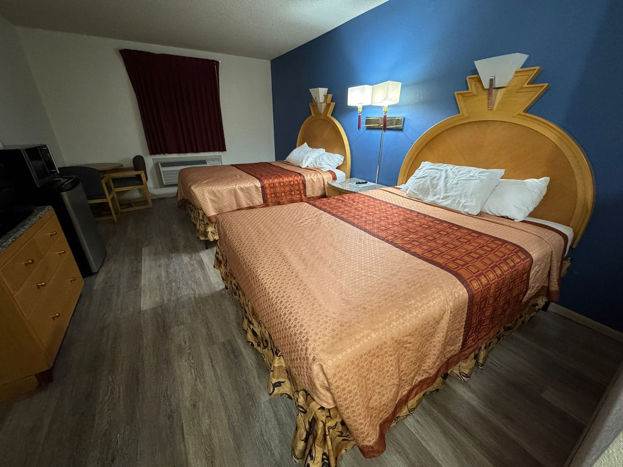 A hotel room with two beds, a desk, a chair, a TV, and a window with curtains.