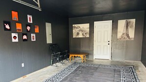 A room with a black wall, a patterned rug, a folding chair, a small wooden table, and several framed pictures.