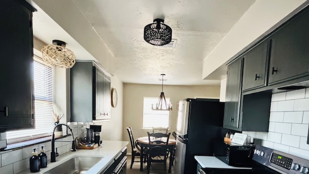 A modern kitchen with dark cabinets, a large island, and a dining area with a chandelier.