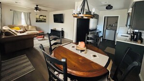 A dining area with a wooden table, chairs, and a chandelier. There is a sofa and a television in the living room area.
