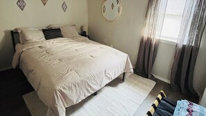 A bedroom with a bed, a ceiling fan, a window with curtains, and wall decorations.