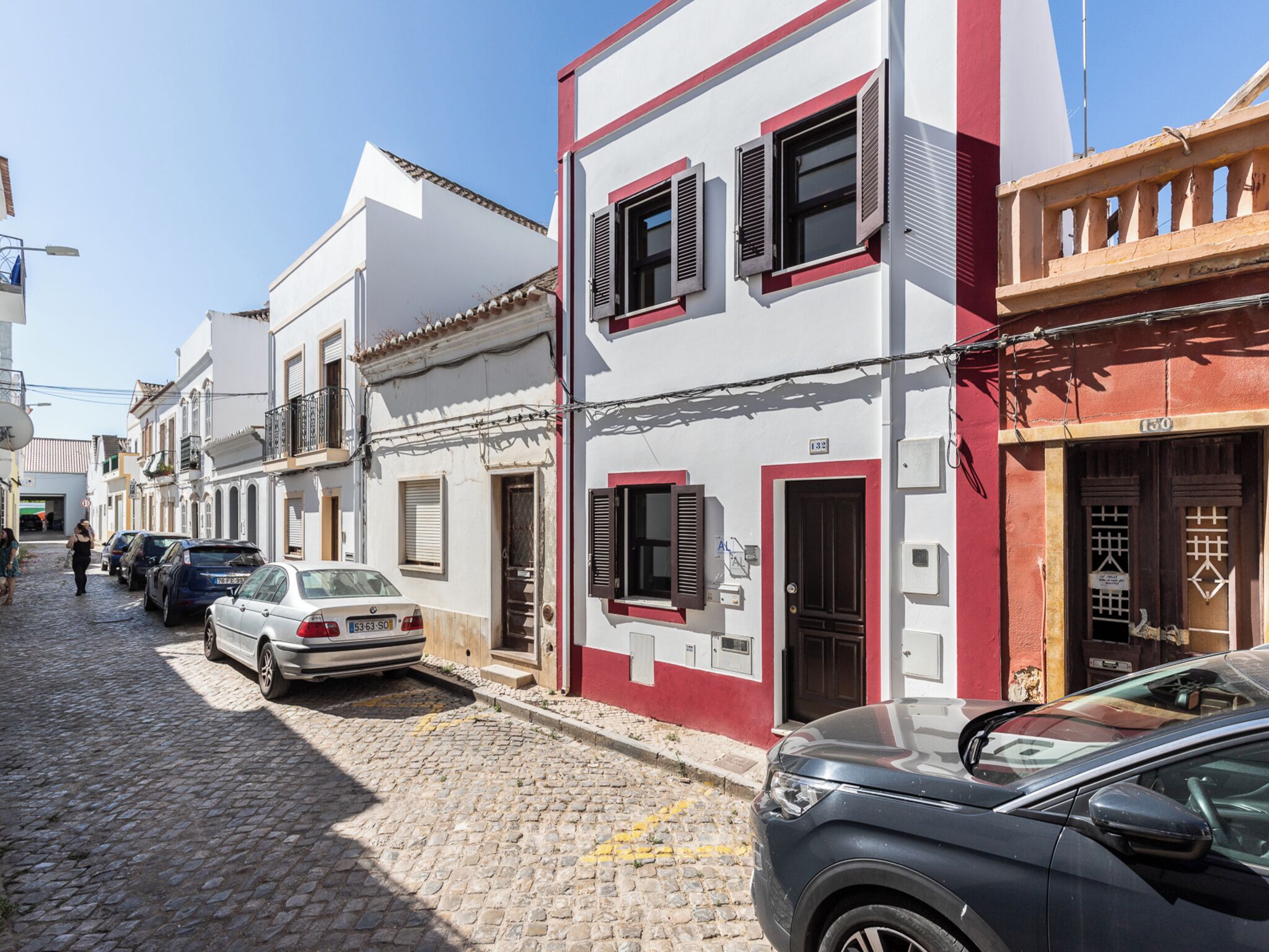 A narrow cobblestone street lined with traditional buildings, some with balconies and shutters.
