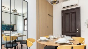 A modern dining area with a round table set for four, surrounded by chairs. A wooden panel wall and a dark door are visible in the background. - Zinnia Villa, Tavira, Algarve (Tavira)