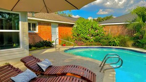 A backyard with a swimming pool, wooden lounge chairs, and a covered patio area. - Big Heated Pool w Sunroom, Centrally-loc. Luxury in Houston, Billiards, Sleeps16 (Houston)