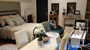A cozy bedroom with a bed, a table with a vase of flowers, and a fireplace. - Au petit bonheur de Séraphine (saint aubin)