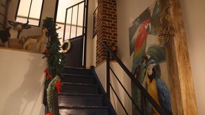 A staircase with a wooden handrail, a Christmas tree with red ribbons, and a mural of colorful parrots on the wall. - Au petit bonheur de Séraphine (saint aubin)