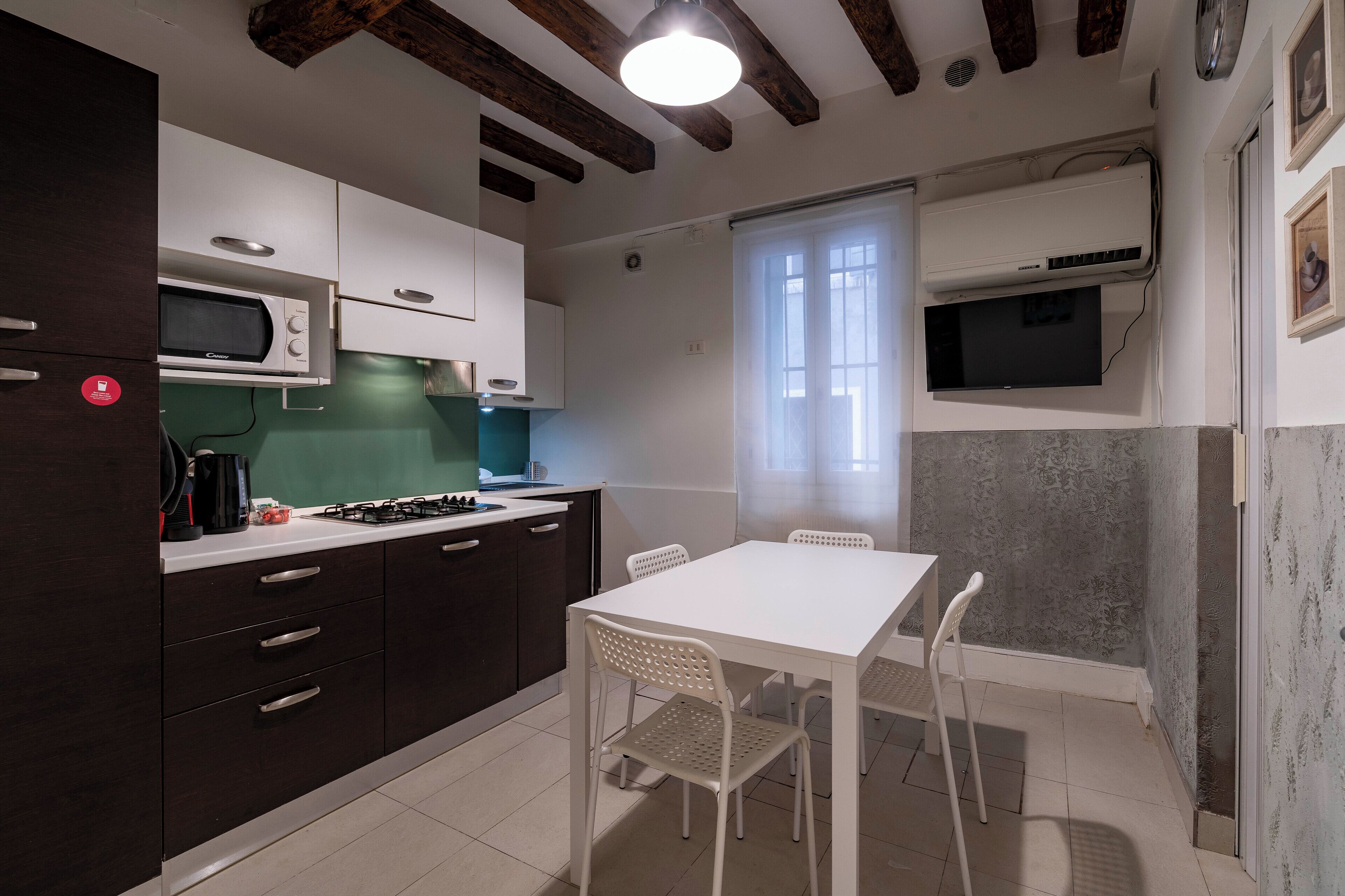A compact kitchen with a microwave, stove, and white cabinets. There is a dining table with chairs and a window with curtains.