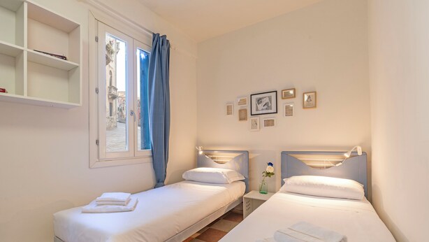 Una habitación de hotel con dos camas individuales, una ventana con cortinas, un estante en la pared y cuadros enmarcados.
