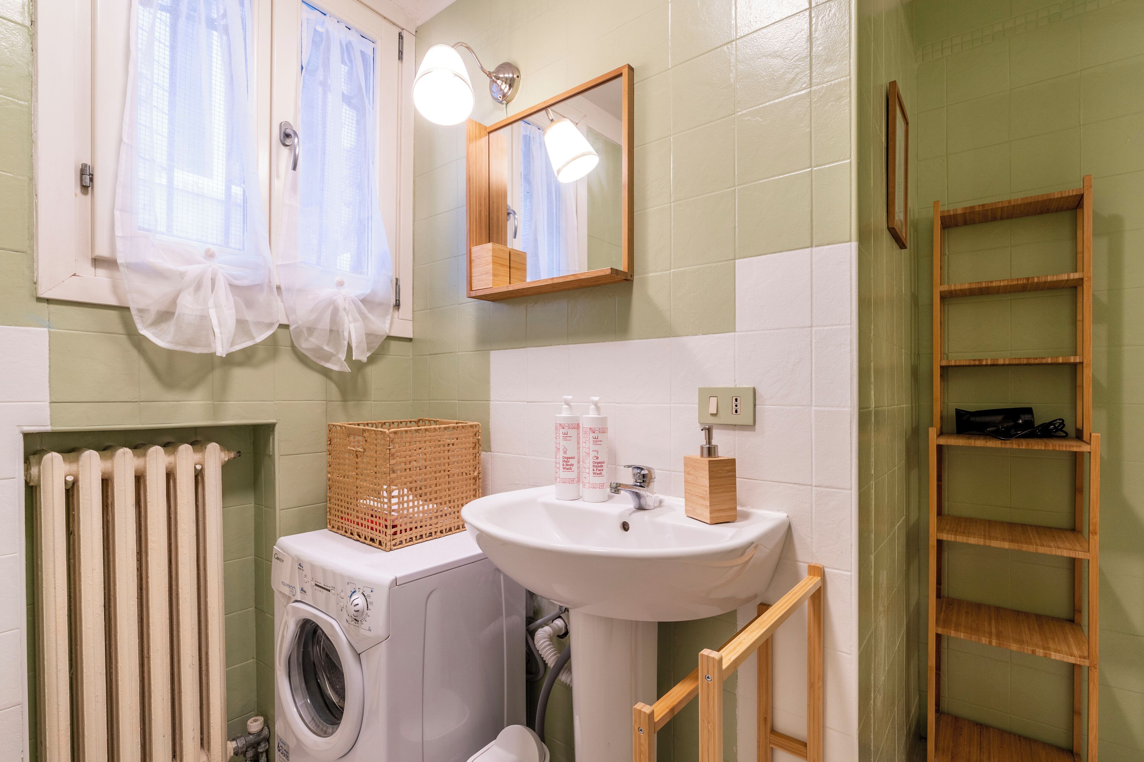 A bathroom with a washing machine, a sink, a mirror, and a wooden shelf.