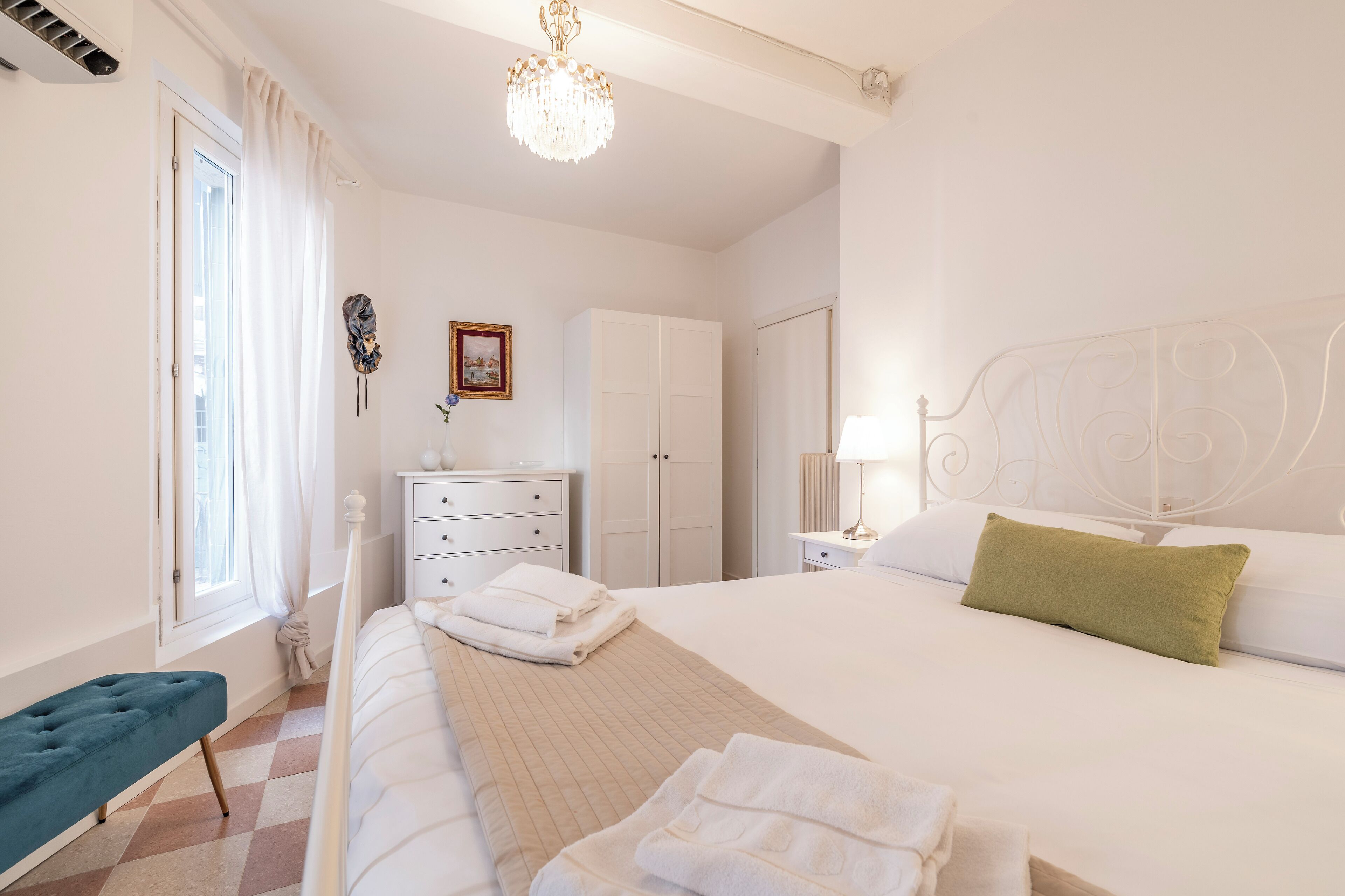 Een hotelkamer met een bed, een bankje, een kledingkast, een bureau en een kroonluchter.