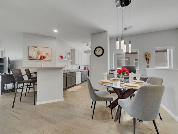 Una cocina moderna con armarios blancos, una zona de comedor con una mesa redonda de cristal y sillas grises.