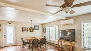 Un coin repas avec une table et des chaises en bois, un ventilateur de plafond et un téléviseur posé sur un meuble en bois.