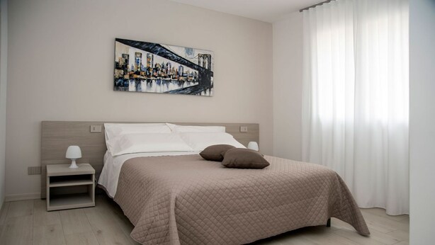 Ein modernes Schlafzimmer mit einem großen Bett, einem Nachttisch, einem Wandbild und einem Fenster mit durchsichtigen Vorhängen.