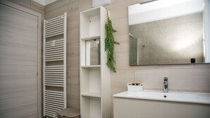 Ein modernes Badezimmer mit Handtuchheizkörper, Toilette, Waschbecken mit Spiegel und Ablagefläche mit Pflanze.