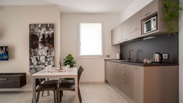 A modern kitchen with a dining area, featuring a large window, a microwave, and a plant. - CAMELOT APARTMENT RED3 (VERONA)