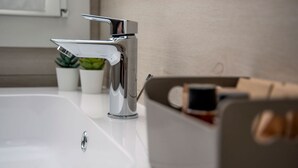 A modern bathroom with a chrome faucet, a white sink, and a box of toiletries. - CAMELOT APARTMENT RED3 (VERONA)