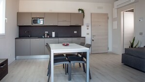 Eine moderne Küche mit grauen Schränken, einer weißen Arbeitsplatte und einer Mikrowelle. Im Wohnbereich befindet sich ein Esstisch mit vier Stühlen und ein graues Sofa.