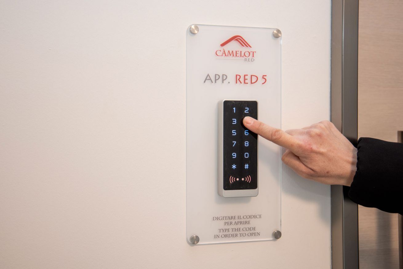 A digital keypad with the label "APP. RED 5" and instructions in Italian for entering a code to open a door.