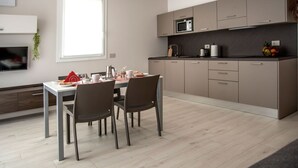 A modern kitchen with a dining table, chairs, and a TV mounted on the wall. - CAMELOT APARTMENT RED4 (VERONA)