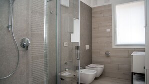 A modern bathroom with a glass-enclosed shower, a toilet, bidets, and a vanity with a mirror. - CAMELOT APARTMENT RED8 (VERONA)