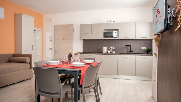 A compact kitchen with a microwave, sink, and cabinets. There is a dining table set with plates and glasses. - CAMELOT APARTMENT RED8 (VERONA)