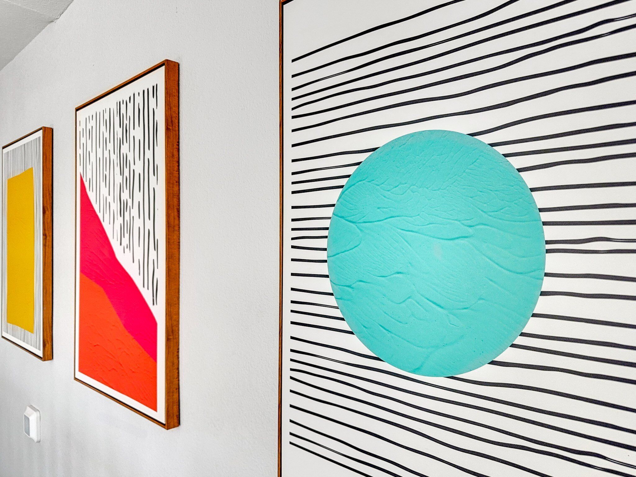 Una pared con tres obras de arte enmarcadas: una con líneas verticales, una con líneas diagonales y una con un diseño circular grande.