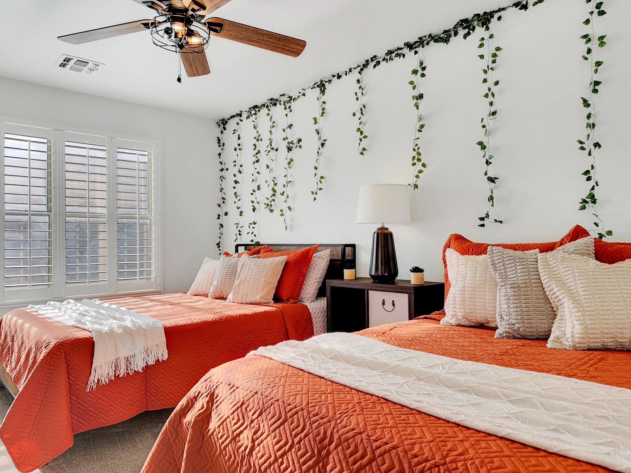 A bedroom with two beds, a ceiling fan, and a window with blinds.
