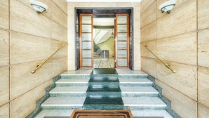 A marble staircase leading to a wooden door with glass panels, flanked by wall sconces and a patterned rug. - Your window overlooking St. Peter's (Roma)
