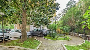 A paved courtyard with a circular bench, surrounded by greenery and parked cars. - Your window overlooking St. Peter's (Roma)