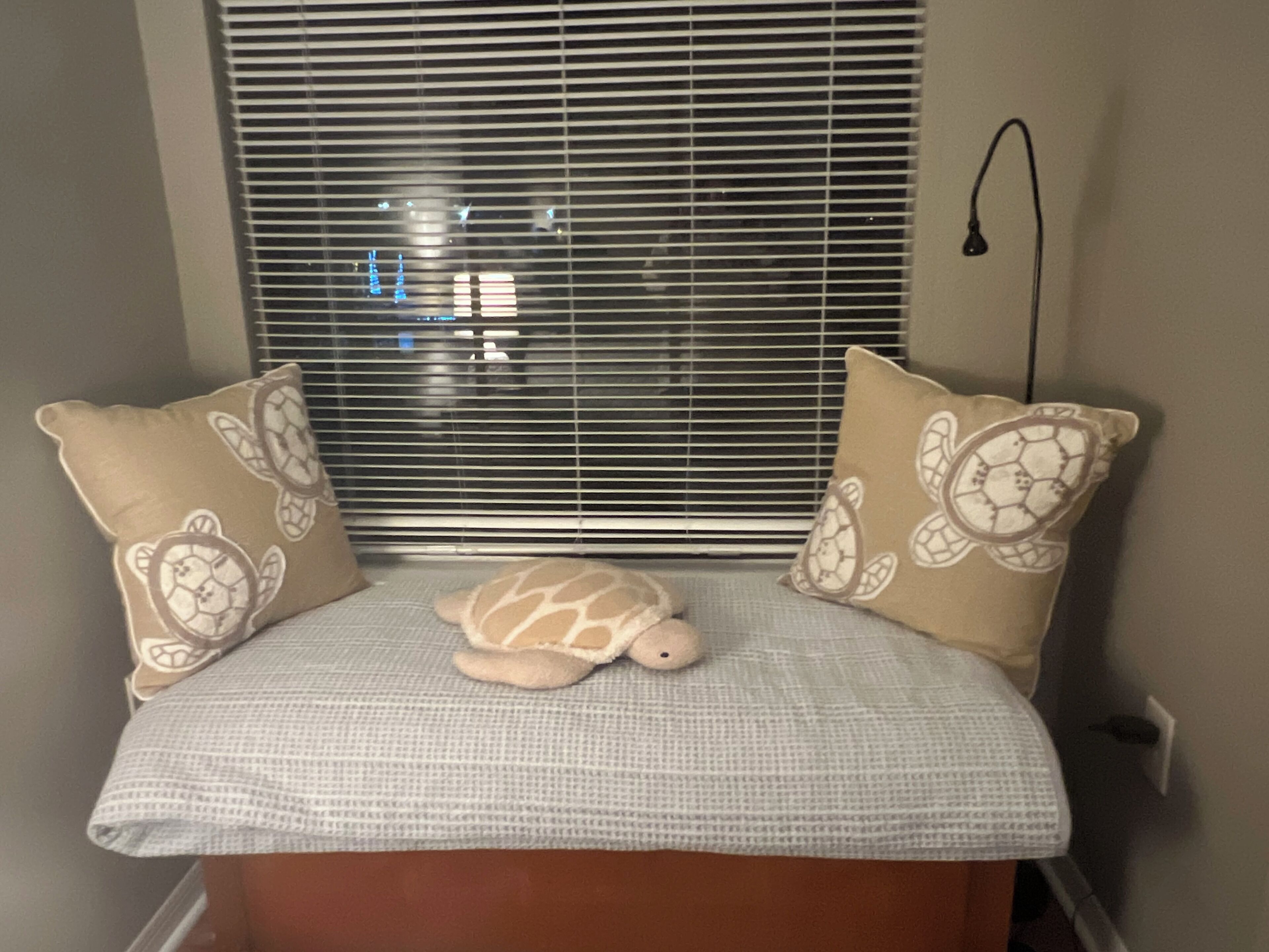 Een bed met een wit geruit beddegoed, twee beige kussens met schildpadmotieven, en een klein pluche schildpaddenspeeltje in het midden.