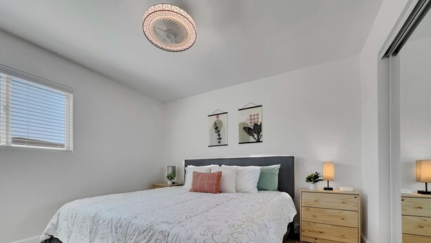A bedroom with a bed, bedside tables, a ceiling fan, and artwork on the wall. - Boulder Apache Junction (Apache Junction)
