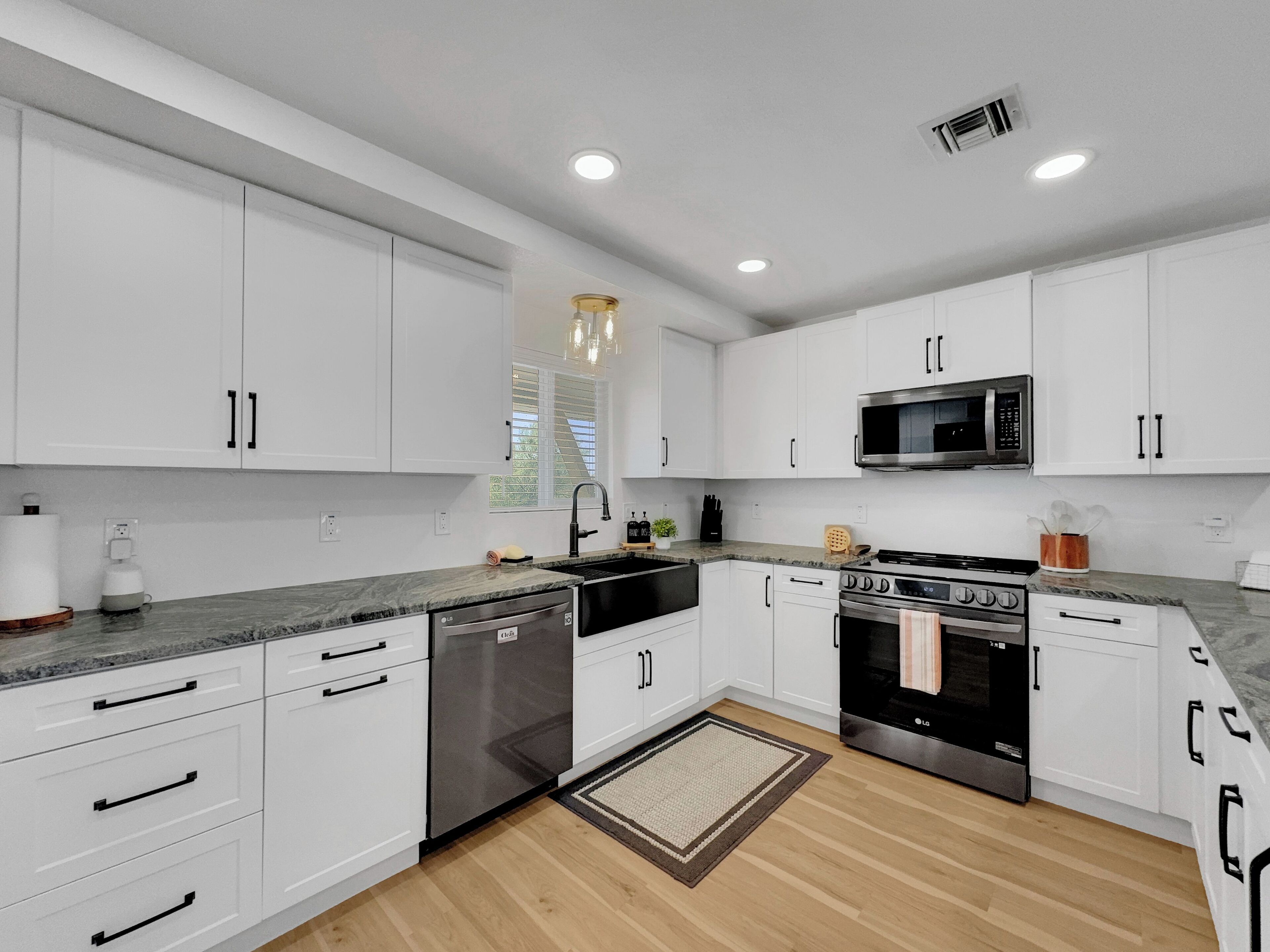 A modern kitchen with white cabinets, a stainless steel microwave, an oven, and a dishwasher.