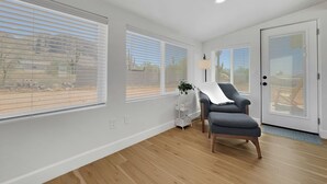 A spacious room with large windows, a grey armchair, a small table with a lamp, and a door with a glass panel. - Boulder Apache Junction (Apache Junction)