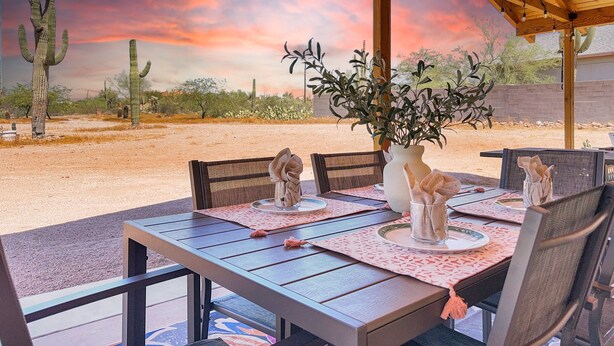 An outdoor dining area with a table set for four, surrounded by chairs, under a wooden pergola with string lights. - Boulder Apache Junction (Apache Junction)
