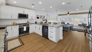 A modern kitchen with white cabinets, a central island, and a dining area with a gray sofa and blue chairs. - Boulder Apache Junction (Apache Junction)