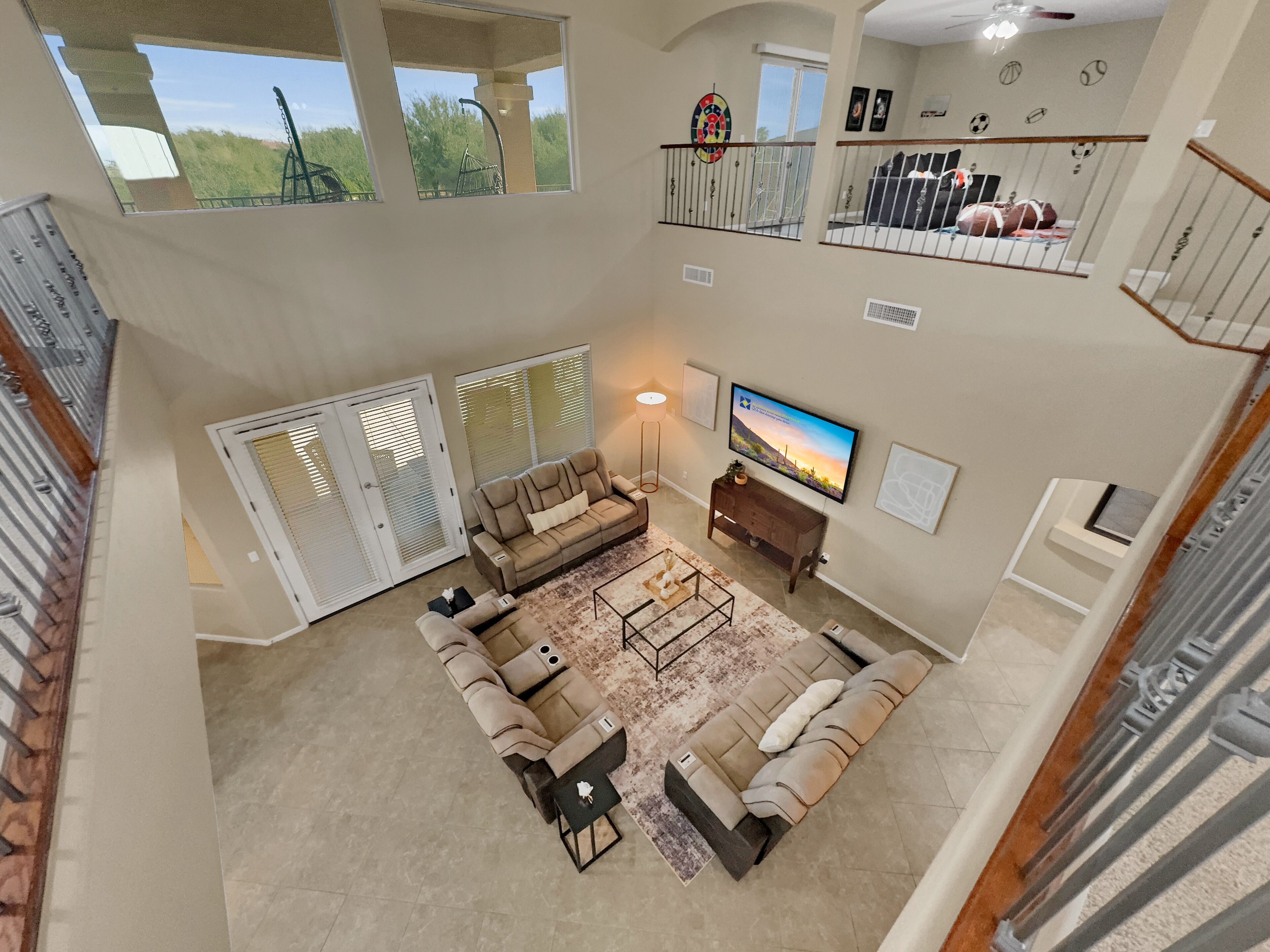 A spacious living area with a large sectional sofa, a flat-screen TV, and a balcony with a view of the outdoors.