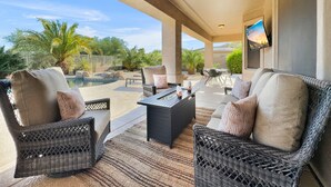 A covered outdoor patio with wicker furniture, a pool, and a TV screen. - Cline Maricopa (Maricopa)