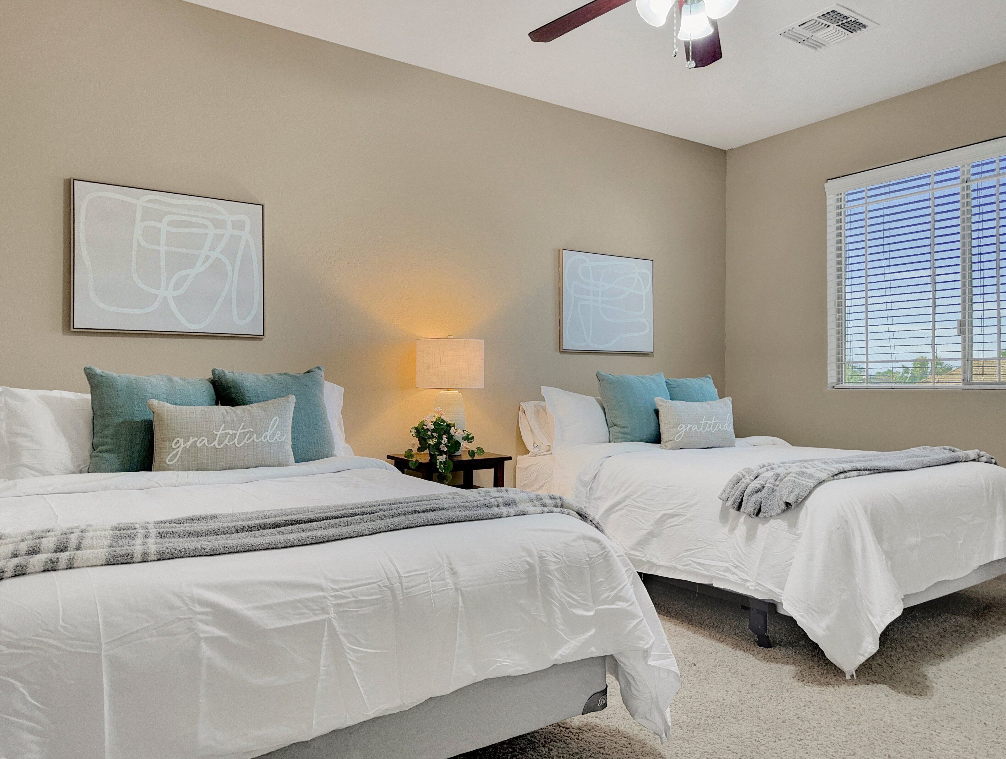 A bedroom with two beds, beige walls, and artwork.