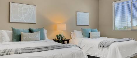 A bedroom with two beds, beige walls, and artwork.