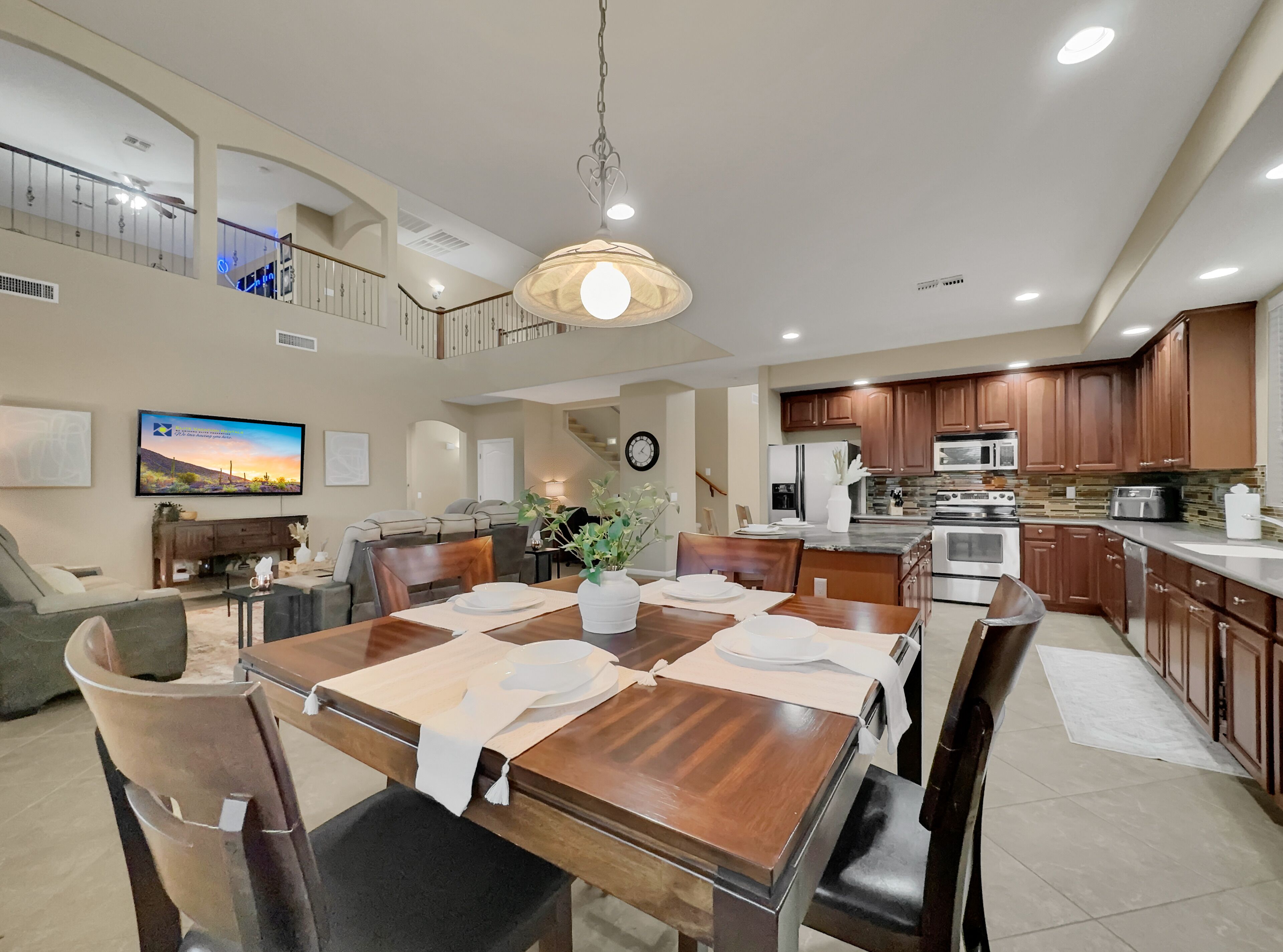 A spacious living area with a dining table set for four, a kitchen with modern appliances, and a balcony with a railing.