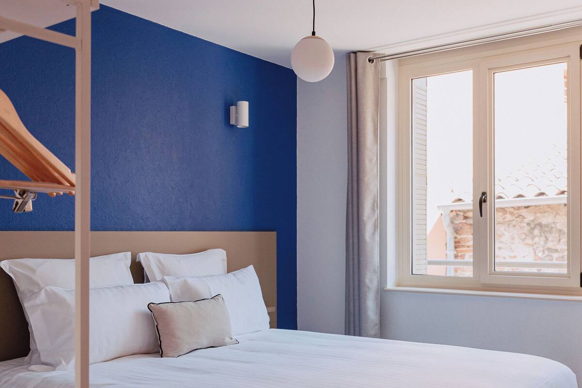 A bedroom with a bed, a wooden headboard, a window with curtains, and a hanging light fixture.