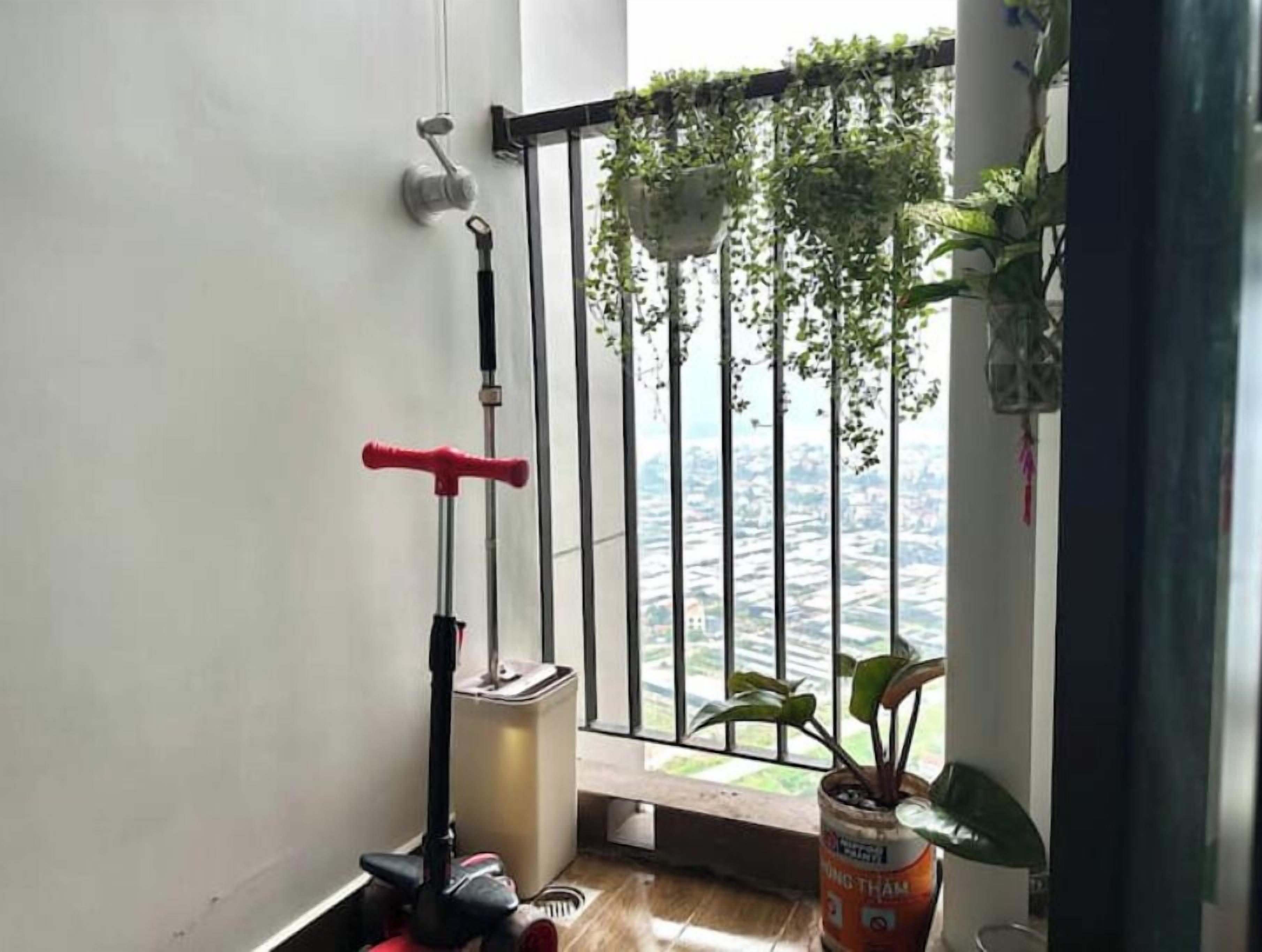 A balcony with a view of a cityscape, a red scooter, a mop, and a potted plant.