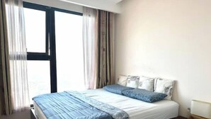 A bedroom with a large bed, a nightstand, and a window with curtains.