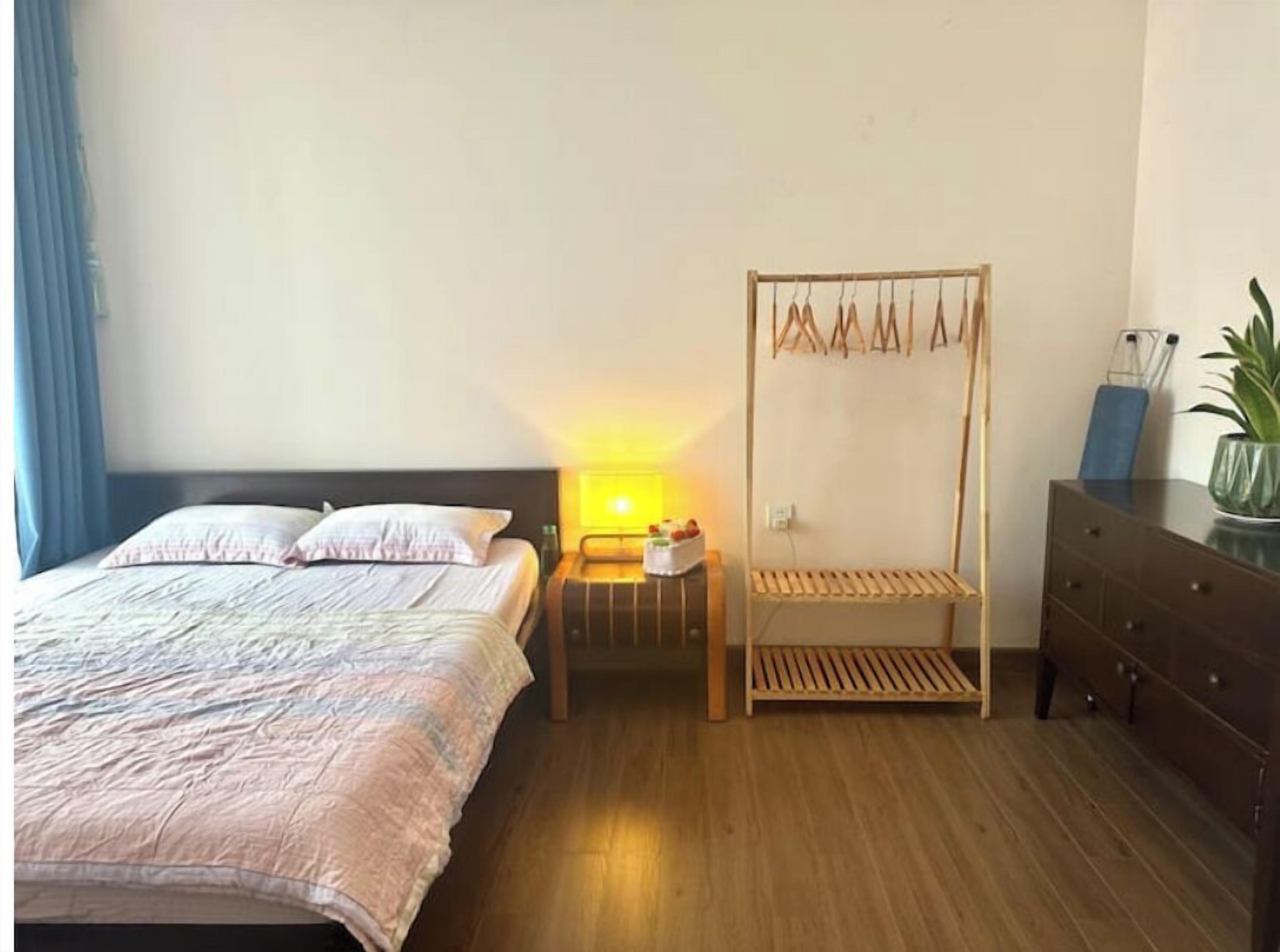 Een slaapkamer met een bed, nachtkastje, lamp, houten plank, kledingkast en een potplant.