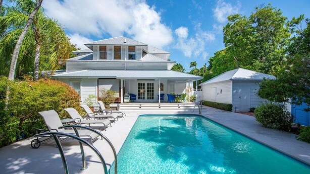 Ein zweistöckiges Haus mit Swimmingpool, Liegestühlen und einer überdachten Terrasse.