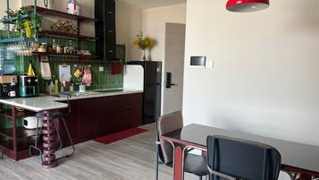 Une cuisine moderne avec un coin repas, comprenant un luminaire suspendu rouge, un tabouret de bar et une table à manger avec des chaises.