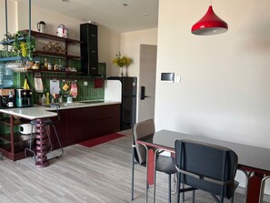 A modern kitchen with a dining area, featuring a red pendant light, a bar stool, and a dining table with chairs.