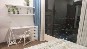 A bedroom with a bed, a desk, and a chair. There is a window with a view of the city at night.