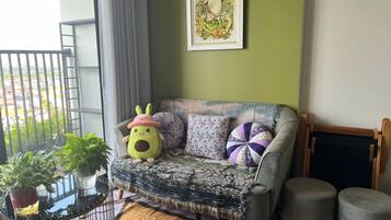 A cozy living area with a sofa, cushions, a small table with plants, and a framed picture on the wall.