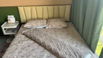 A bed with a patterned bedspread, two pillows, a nightstand with a calendar, and a green wall.
